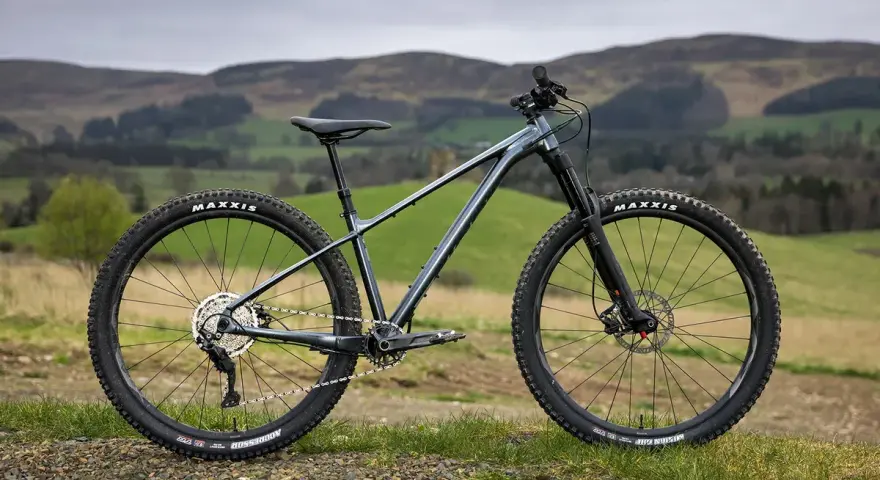 A dark grey hard tail bike with knobby tires sits on a grassy hill, ready for adventure.