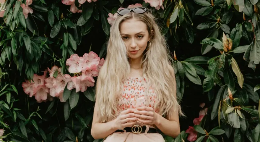 Blondynka w kwiecistej sukience, z okularami na głowie, otoczona różowymi kwiatami rododendronów. To kwintesencja słowiańskiej urody.
