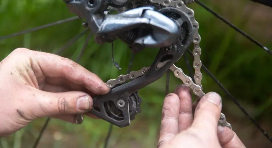 Smutsiga händer arbetar med att byta kedja på en cykel. Detaljbild på bakväxeln och kedjan.