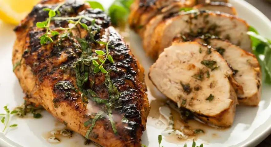 Delicioso pollo a la parrilla jugoso y tierno, con hierbas frescas y limón, servido en un plato blanco.
