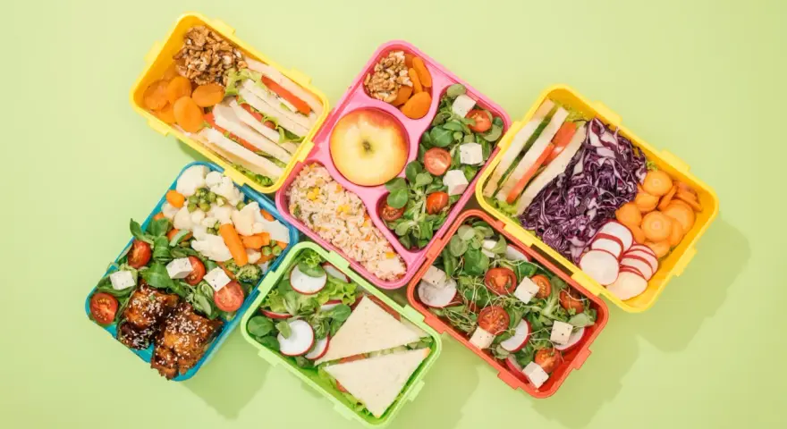 Kolorowe pojemniki na lunch z kanapkami, sałatkami, owocami i warzywami.