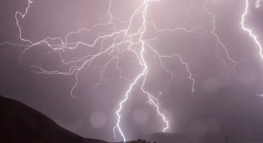 Éclairs zébrant un ciel sombre, illuminant un paysage montagneux lors d'un photo d'orage spectaculaire.
