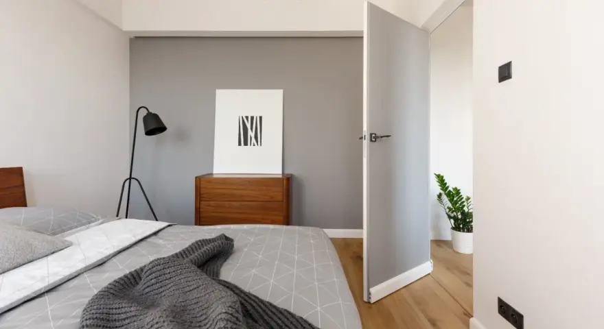 Nowoczesna sypialnia z łóżkiem, komodą i lampą. Idealne miejsce na wynajem krótkoterminowy.