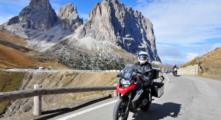 Motocyklista przemierza malowniczą drogę w Dolomitach. Pogoda dopisuje, a widoki zapierają dech w piersiach.