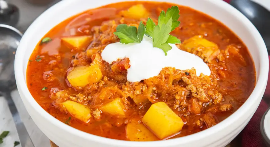 Herzhafte Mitternachtssuppe mit Hackfleisch und Sauerkraut, garniert mit einem Klecks Sauerrahm und Petersilie.