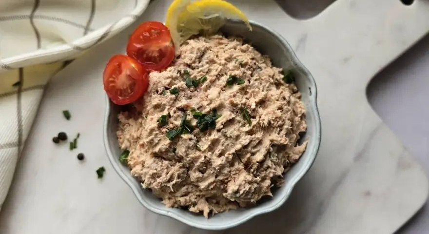 Un bol de rillettes de thon, garni de tomates cerises et de quartiers de citron, prêt à être dégusté.