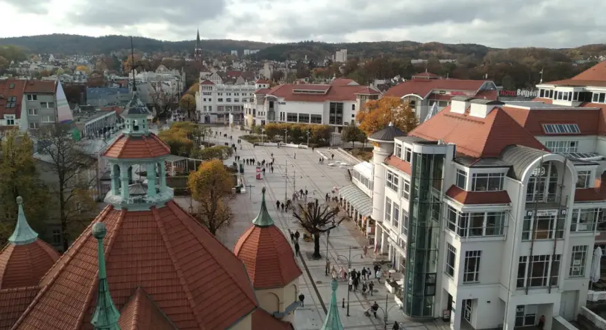 Widok na plac w Sopocie z charakterystycznymi dachami i budynkami. Wiele osób spaceruje, szukając sopotorium opinie.