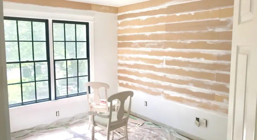Room in progress, showing how to install shiplap on the wall. Two chairs sit on protective plastic sheeting.