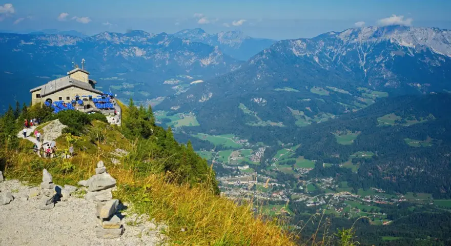 View from Hitler's Eagle's Nest, a stone building with blue umbrellas, perched high in the Bavarian Alps overlooking a valley.