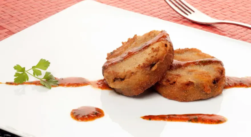 Dos manitas de cerdo rebozadas y fritas, servidas con salsa roja y perejil en un plato blanco.