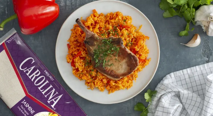 Chuleta de cerdo jugosa sobre arroz rojo con pimientos.