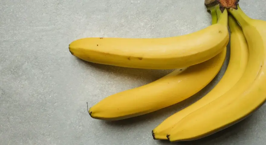 Trzy żółte banany leżą na szarym tle. Jeden duży banan kcal to świetna przekąska.