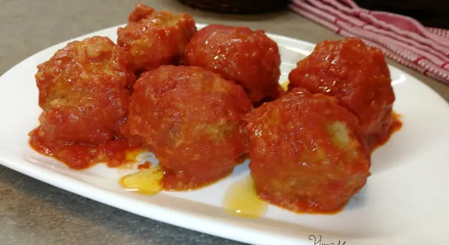 Polpette di pane al sugo, morbide e saporite, servite su un piatto bianco. Un classico della cucina italiana.