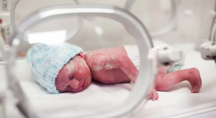 Maleńki noworodek, dziecko urodzone w 20 tygodniu ciąży, w inkubatorze, w niebieskiej czapeczce.