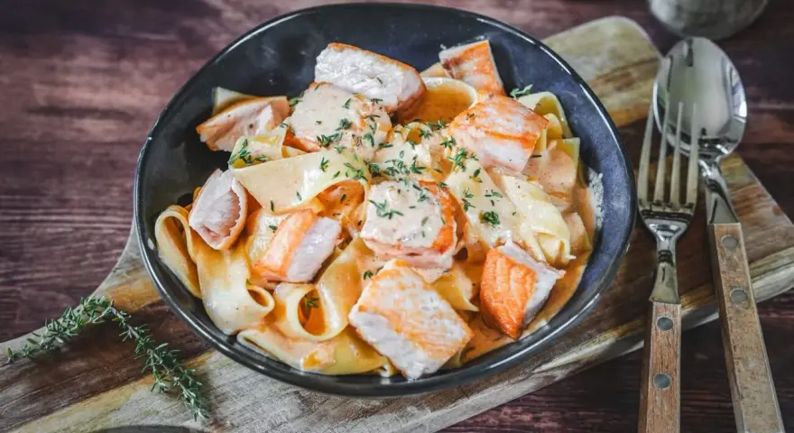 Breite Bandnudeln mit saftigen Lachs-Stücken in cremiger Lachs Sahne Sauce, garniert mit frischen Kräutern. Ein Genuss!