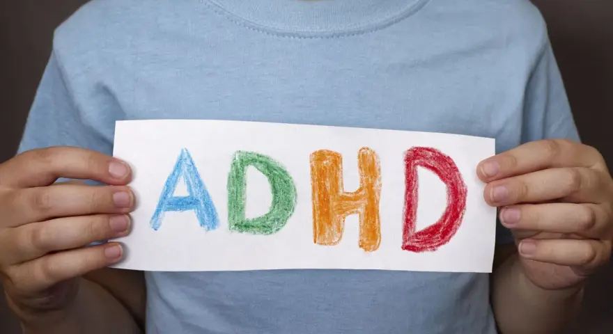 Mani di bambino tengono un foglio con la scritta "ADHD" colorata. Riconoscere i sintomi dell'ADHD è il primo passo.