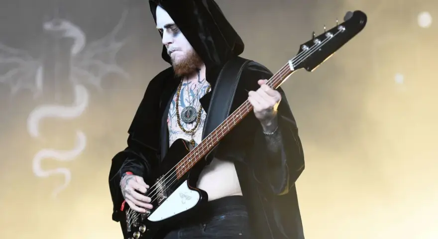 Le bassiste d'un groupe metal connu, maquillé et tatoué, joue sur scène, drapé dans une cape noire.