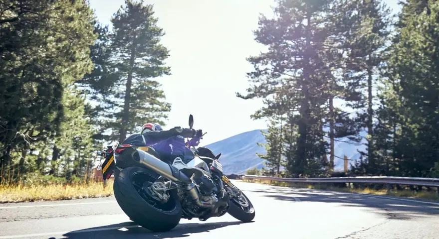 Motocyklista na zakręcie, otoczony lasem, z dumą prezentuje opony Pirelli. Jazda w stylu Pirelli klub.