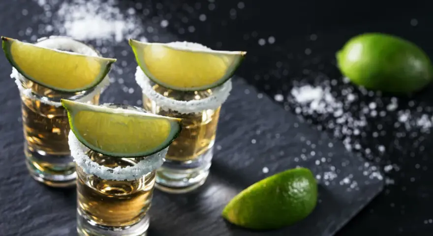 Szklanki z tequilą, ozdobione solą i ćwiartkami limonki. Idealne do picia z limonką, gdy zastanawiasz się, z czym pić tequilę.