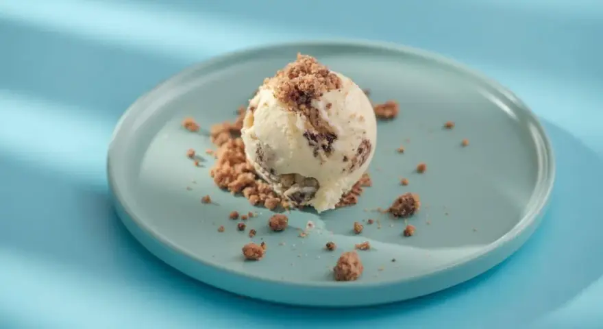 Eiscreme mit Schokoladenstückchen und Krümeln, serviert auf einem blauen Teller. Glukosesirup sorgt für die cremige Konsistenz.