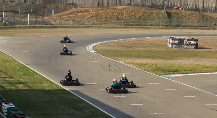 Gara di go-kart su pista con piloti in azione. Sullo sfondo, un cartellone pubblicitario con la scritta "Ottobiano Motorsport".