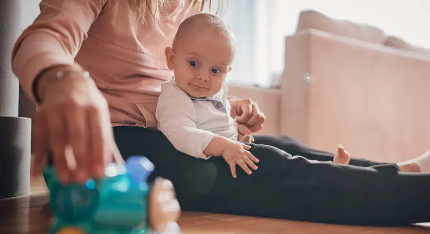 Mama bawi się z 9-miesięcznym dzieckiem, podając mu kolorową zabawkę-pociąg.