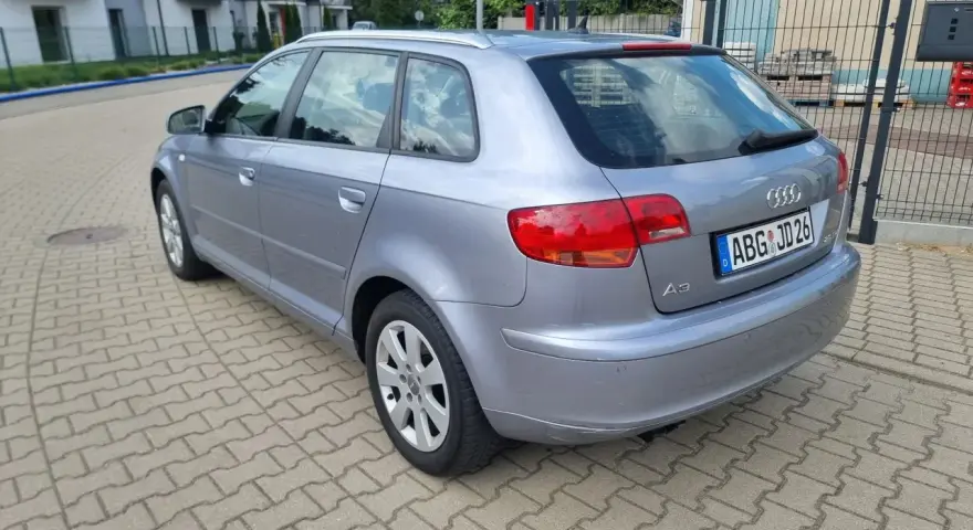 Srebrny Audi A3 kombi zaparkowany na kostce brukowej, w tle domy i drzewa.