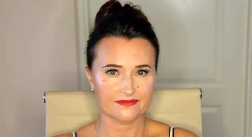 Kobieta z upiętymi włosami prezentuje perfekcyjny makijaż wieczorowy. Czerwone usta i podkreślone oczy dodają jej uroku.
