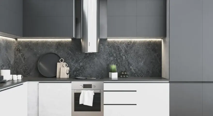 Moderna cocina blanca y gris oscuro con campana extractora de acero inoxidable, encimera de piedra y armarios minimalistas.