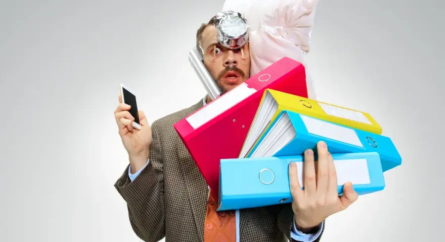 Uomo stressato con pile di cartelle, telefono e cuscino in testa. Lo stress aumenta il cortisolo, che fa ingrassare.