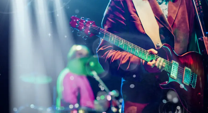 Koncertowe emocje! Gitarzysta gra na scenie, przypominając najlepsze zagraniczne zespoły lat 90. W tle perkusista.