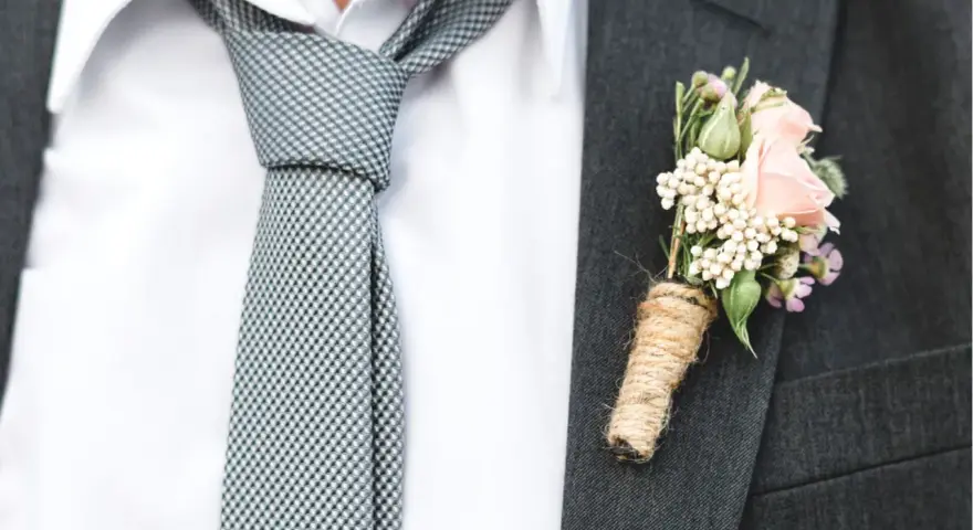 Elegancki krawat do ślubu w kratkę, biała koszula i butonierka z różową różą.