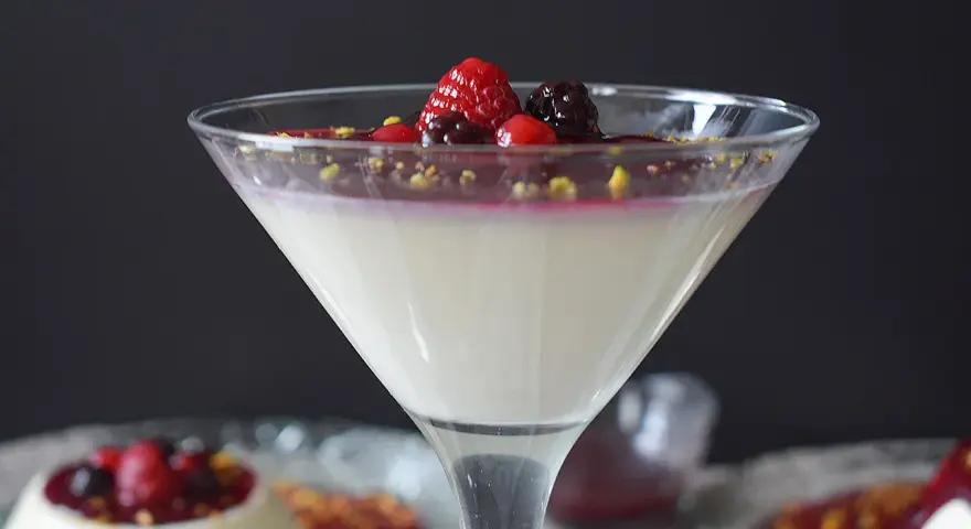 Deliciosa panna cotta receta, cremosa y adornada con frutos rojos y pistachos. Un postre elegante.