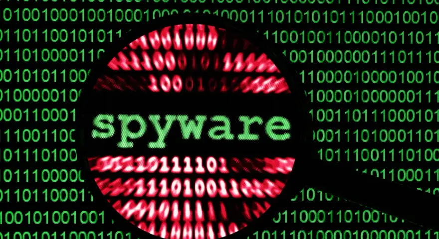 Lupa sobre código binario verde y rojo, con la palabra "spyware" en verde en el centro.