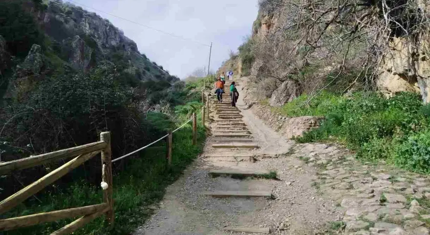 Senderos de montaña con escalones de piedra y madera. Personas caminan por las rutas Patones de Arriba, rodeadas de vegetación y acantilados.