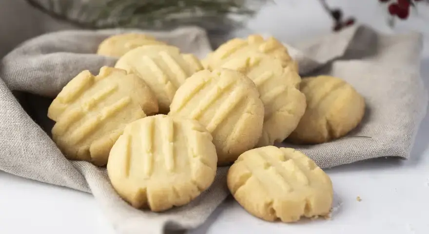 Montón de galletas de mantequilla doradas con líneas marcadas, servidas sobre una tela gris.