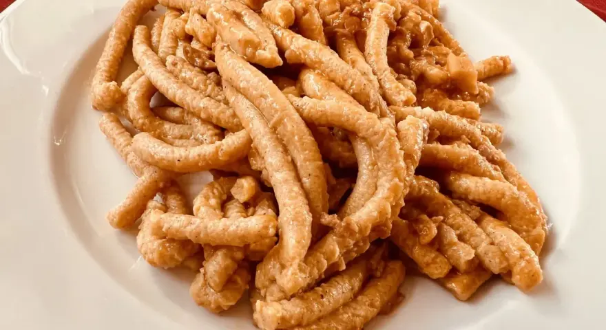 Pici all'aglione, uno dei piatti tipici di Arezzo, serviti su un piatto bianco.