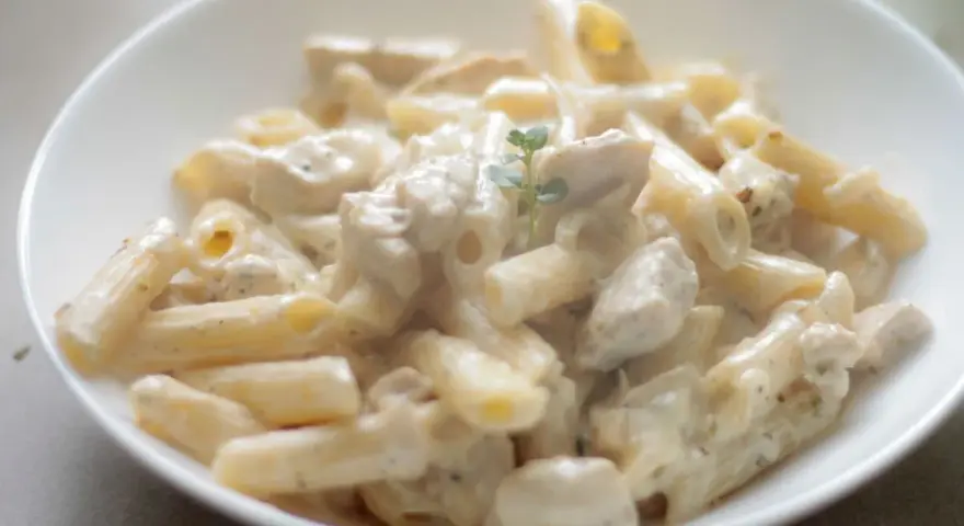 Penne z kurczakiem w kremowym sosie, udekorowane gałązką ziół. Pyszne danie, które zachwyci każdego smakosza.