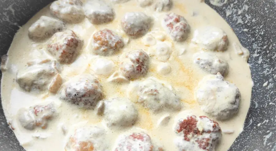 Pyszne klopsiki w sosie śmietanowym, gotujące się na patelni. Aromatyczne danie, które zachwyci każdego.