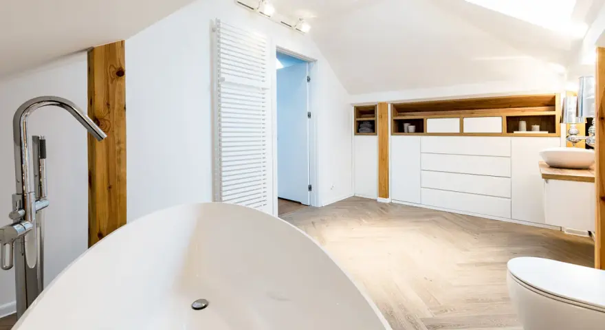 Élégante salle de bain sous pente avec baignoire îlot, lavabo, toilettes et rangements en bois.