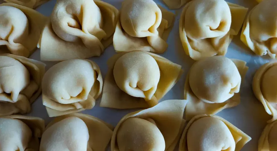 Surowe tortellini ułożone rzędami na jasnym tle.