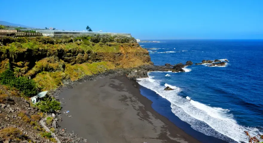 Spiaggia di sabbia nera e scogliere verdi sulle isole delle Canarie, con il blu intenso dell'oceano Atlantico.
