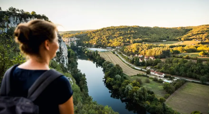 Une femme admire un paysage de carte postale lors de son voyage découverte en France. La rivière serpente à travers des collines verdoyantes et des villages pittoresques.