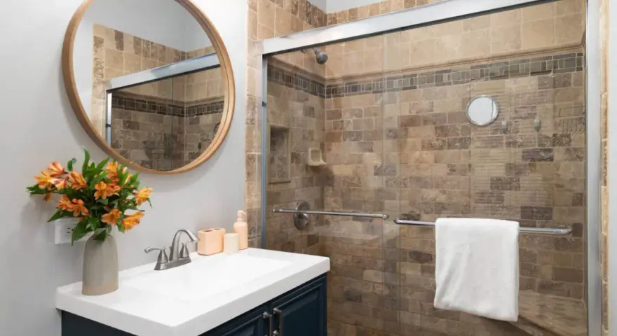 Salle de bain moderne avec douche carrelée, lavabo et miroir rond. Idéal pour nettoyer VMC et profiter d'un espace sain.