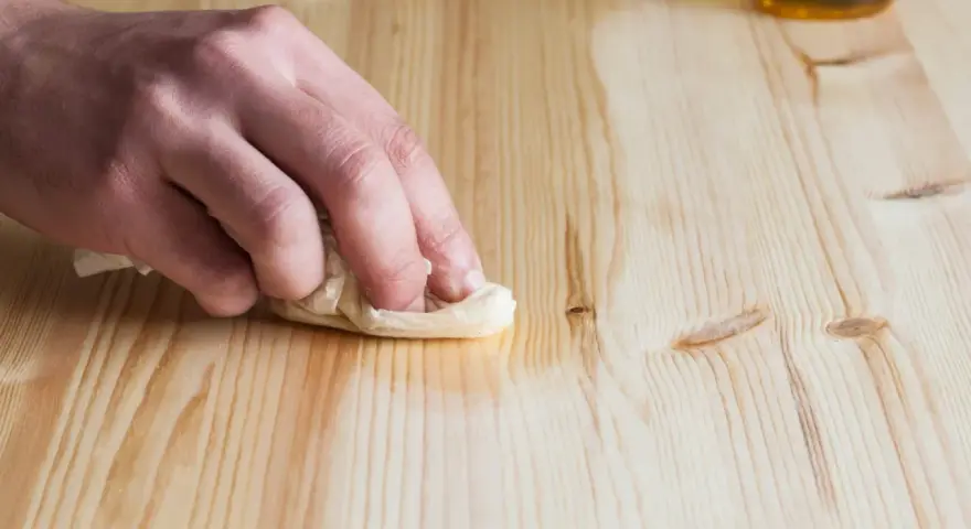 Main d'une personne nettoyant une table en bois avec du vinaigre blanc et un chiffon.