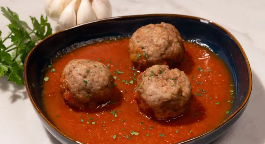 Tres albóndigas caseras en una rica salsa de tomate, adornadas con perejil fresco. Un plato reconfortante que evoca la cocina tradicional.