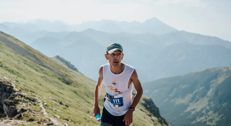 Zawodnik z numerem 111 biegnie pod górę podczas Tatra Sky Marathon. W tle piękne, mgliste pasmo górskie.