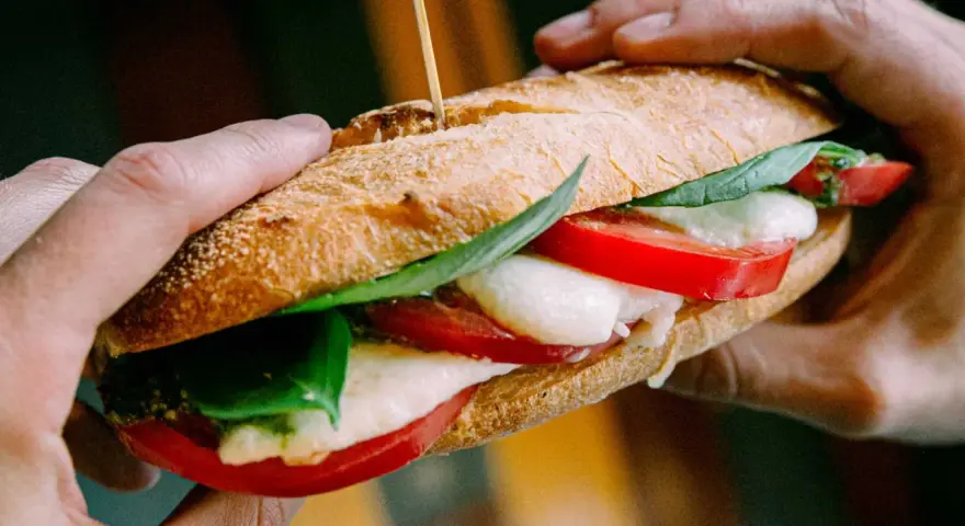 Ręce trzymają pyszne włoskie pieczywo z mozzarellą, pomidorami i bazylią. Idealne na szybki lunch.