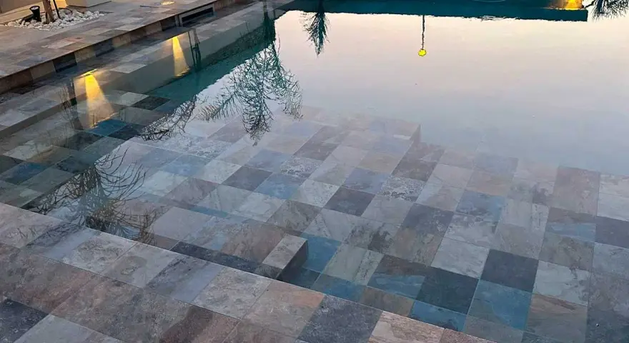 Escalones de piscina con diversos tipos de gresite para piscinas, creando un mosaico de tonos grises, azules y marrones.