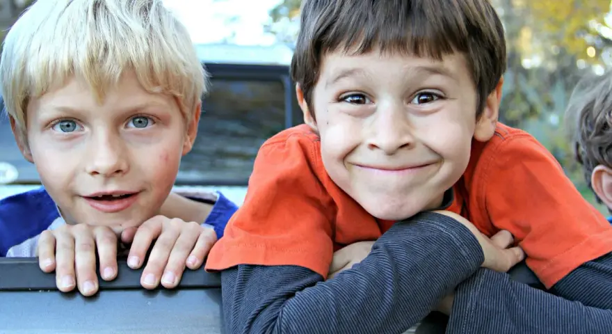 Dwóch chłopców, jeden z blond włosami i niebieskimi oczami, drugi z brązowymi włosami i szerokim uśmiechem. Ich żywe spojrzenia mogą przypominać objawy ADHD u 2 latka, pełne energii i ciekawości świata.